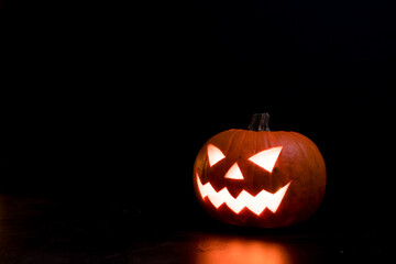 Moody scary Halloween pumpkin jack o'lantern with glowing eyes on dark background