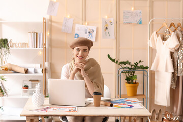 Young female clothes stylist with modern laptop in studio