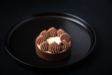 Tarte Schoko-Cheesecake. Feiner Cheesecake mit natürlicher Vanilleschote und einer haube aus Schokolade. Schrarze Hintergrund. 