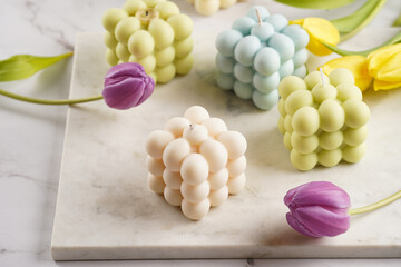Many bubble candles - off-white, beige-colored and blue - on marble board with spring flowers - yellow and purple tulips