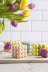Many bubble candles - off-white, beige-colored and blue - on marble board with spring flowers -...