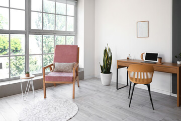 Stylish pink armchair and table with computer in interior of room