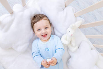 happy smiling baby boy in crib in blue bodysuit, cute joyful little baby in bedroom