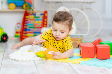 baby boy plays in the children's room in a yellow bodysuit with bright colorful toys