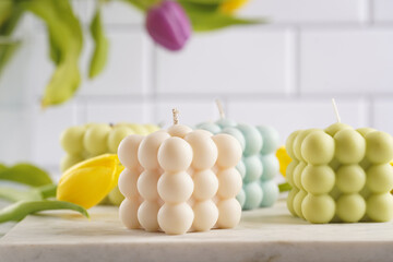 Many bubble candles - off-white, beige-colored and blue - on marble board with spring flowers tulips