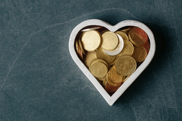 Euro coins in heart shaped white box on dark stone background with copy space