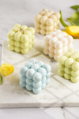 Many bubble candles - off-white, beige-colored and blue - on marble board with spring flowers tulips