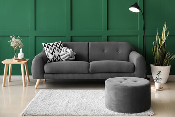 Comfortable pouf, sofa, table and floor lamp near color wall
