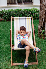 a laughing boy is lying on a folding chair on a chaise longue outside