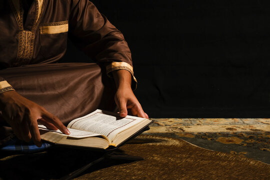 Selective Focus Picture Of A Men Reading Holy Quran On Copyspace Dark Background. Quran Hour And Nuzul Quran Concept.