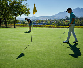 Putting the whole day. Shot of two focused young men playing a game of golf outside on a golf...