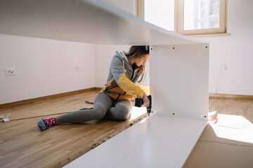 Low angle view of woman using cordless screwdriver for assembling furniture