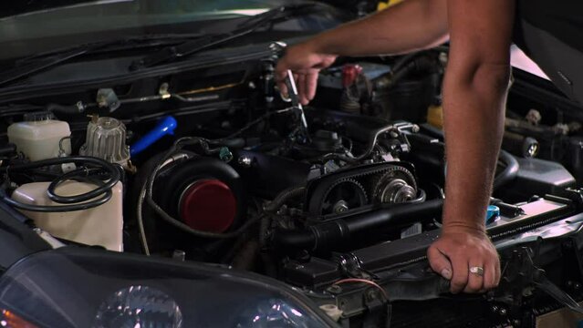 Mechanic spins with a wrench under the hood of a car. Tuning JZ turbo engine. Man works in a car service.
