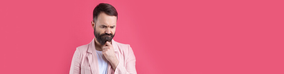 Fototapeta premium Handsome man with a beard in a pink jacket is thinking over an isolated red background.