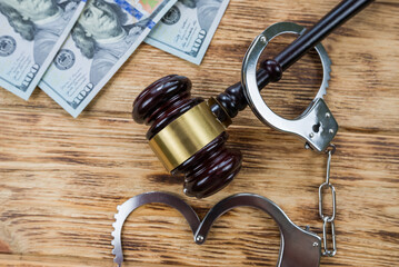judge's gavel, dollars and handcuffs on a table.