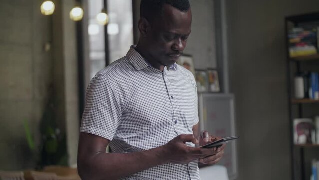 Side view of one happy black African businessman typing on the mobile phone standing indoor people using smartphone