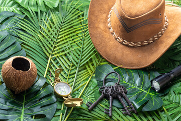 Concept of treasure hunt and travel adventures, hat, compass, flashlight, a bunch of old keys on a background of tropical leaves,