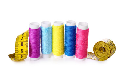 Multicolored thread spools and measuring tape on white background