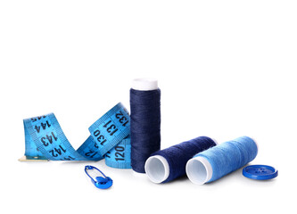 Blue thread spools, button, measuring tape and safety pin on white background