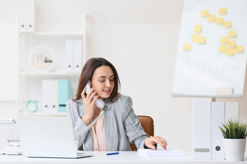 Young secretary talking by phone while working in office