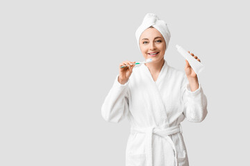 Beautiful mature woman in bathrobe, with tooth brush and paste on light background