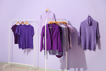 Racks with clothes in purple shades near lilac wall