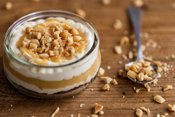 Snickers toffee cream peanut layered dessert in a glass jar on a wooden background - obrazy, fototapety, plakaty