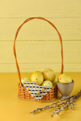 Wicker basket of painted Easter eggs and pussy willow on yellow background