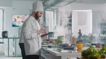 Male cook analyzing culinary recipe on digital tablet in kitchen, using internet on gadget to prepare food. Professional chef in uniform cooking gourmet meal from online gastronomy website. - Powered by Adobe