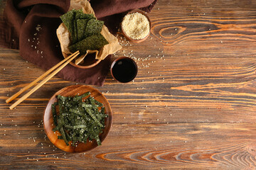 Plate and bowl of tasty seaweed sheets with sesame on wooden background