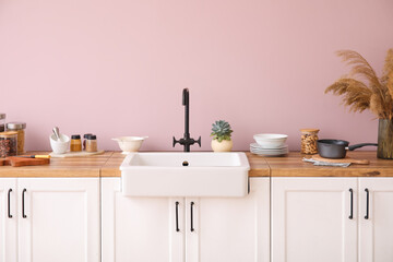Counters with sink, kitchen utensils and pampas grass in vase near pink wall