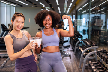 Asian and African American woman finishing workout and drinking protein milk shake vitamins after...