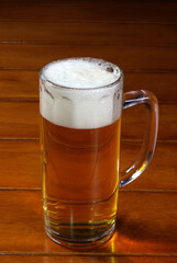 One glass mug with lager or porter is delicious frothy beer on a wooden tabletop a sunny day.