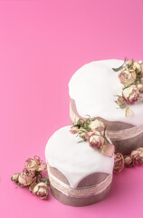 Glazed Easter cakes decorated with dry tea rose flowers on bright pink background. Easter composition with cakes, roses and chocolate eggs. Holiday background with copy space for your design.