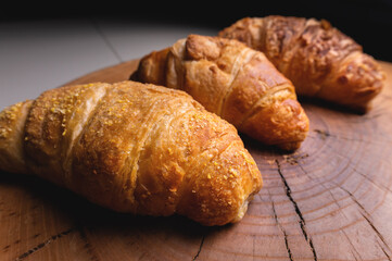 Three French croissants on a wooden cutting board in contrasting light. Fresh treats for breakfast