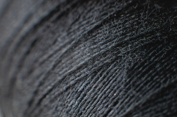 Dark gray spool of thread at extremely high magnification and shallow depth of field. Textile background
