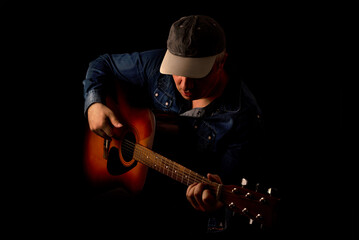 Session guitar player in a jeans shirt plays an acoustic guitar shot on black background. Low key portrait.