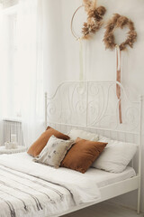 Wrought iron white bed in a cozy light bedroom with many pillows and linens from ecological natural materials