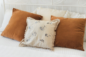 Pillows on the bed in cozy bedroom from natural ecological materials linen and velvet. Details of trendy and eco-friendly living room in light beige and brown earth colors.