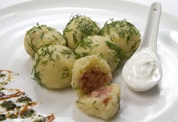 Potato dumplings stuffed with meat with dill on a white bowl.