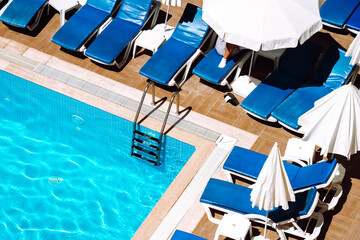 View of a part of a swimming pool and deck chairs in economy hotel. Summer concept. Relaxing chairs with pillows beside swimming pool