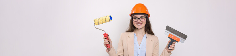 Girl engineer in an orange construction helmet with plastering painting tools in her hands on a white background.