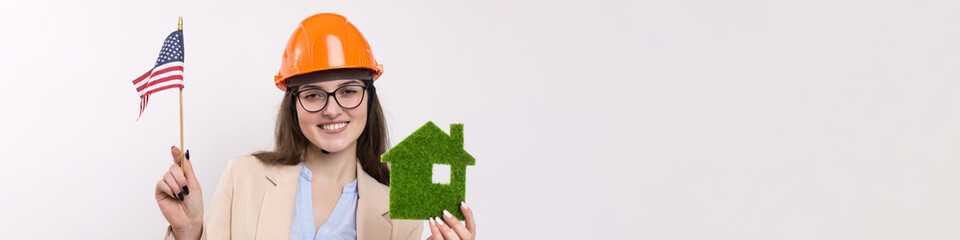 A girl in a construction helmet and an American flag holds a green eco house.