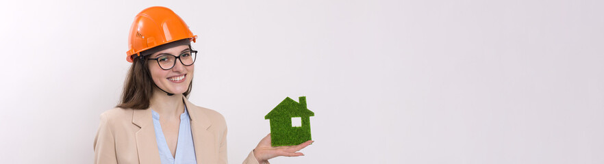 A girl in a construction helmet holds a green house. The concept of ecological clean housing.