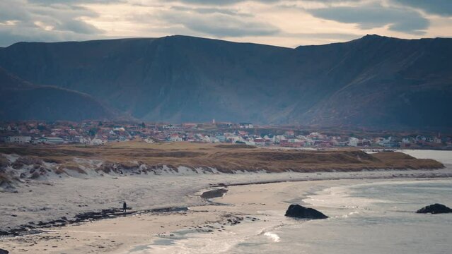 A sandy shores near the village of Bleik on the Andoya island. Norway. A lonely passerby on the beach. Waves roll slowly. Slow-motion, pan left.