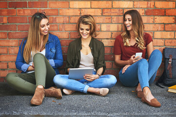 Fototapeta na wymiar Wifi lets them study anywhere on campus. Shot of three smiling female university students sitting together outside on campus using a digital tablet.