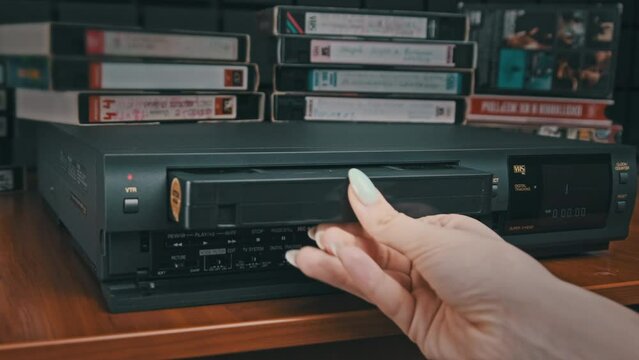 Insert VHS cassette into VCR and push play button. Black vintage videotape cassette recorder with counter on desk with many video cassettes. Inserting old VHS Tape into retro player. Home video archiv