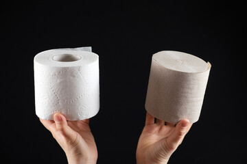 Two types of toilet paper in the hands of a person - white soft paper and gray from waste paper on a black background