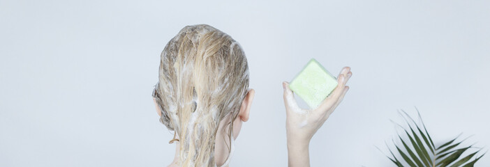 Solid hair shampoo. Close-up of a blonde girl in the bathroom, which lathers her hair with dry...