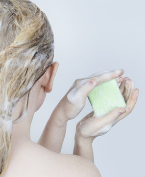 Solid Hair Shampoo. Close-up Of A Blonde Girl In The Bathroom, Which Lathers Her Hair With Dry Shampoo. Lots Of Foam And Peek Effect.